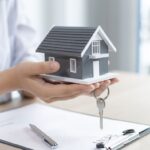 person holding a house with a key and clip board